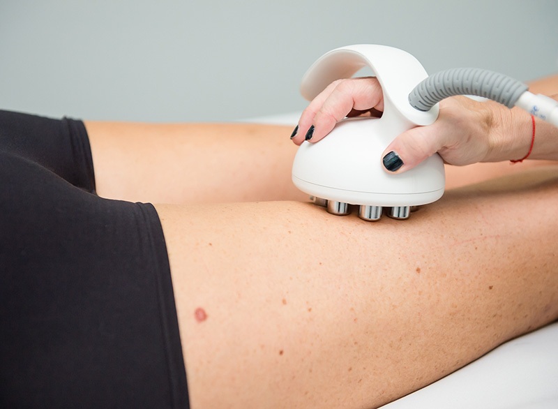 Cosmetologist reducing cellulite on hips of female patient, using ultrasound cavitation machine. Cropped shot of a woman getting rf lifting treatment on back of her legs by professional beautician.