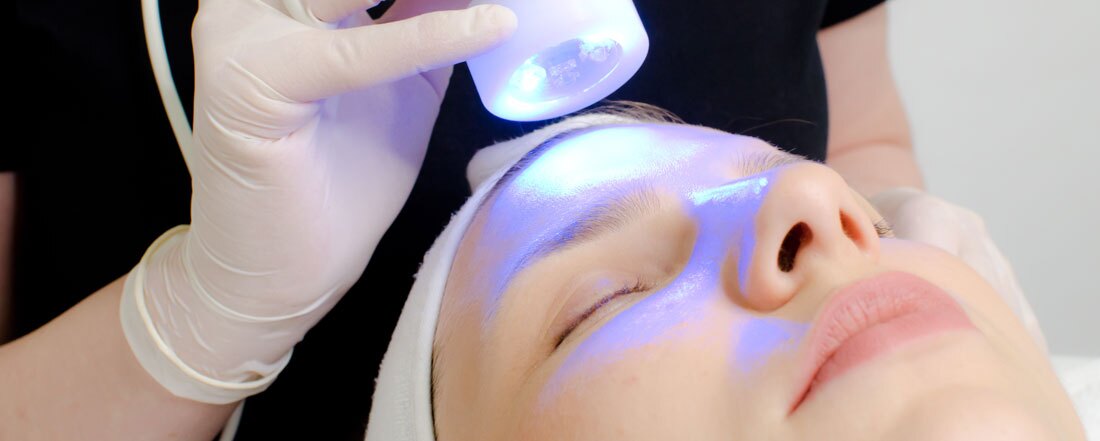 beautician applying blue led light therapy to female customer in beauty salon, facial photo therapy for skin pore cleansing. Anti-aging treatments and photo rejuvenation procedure extreme close up